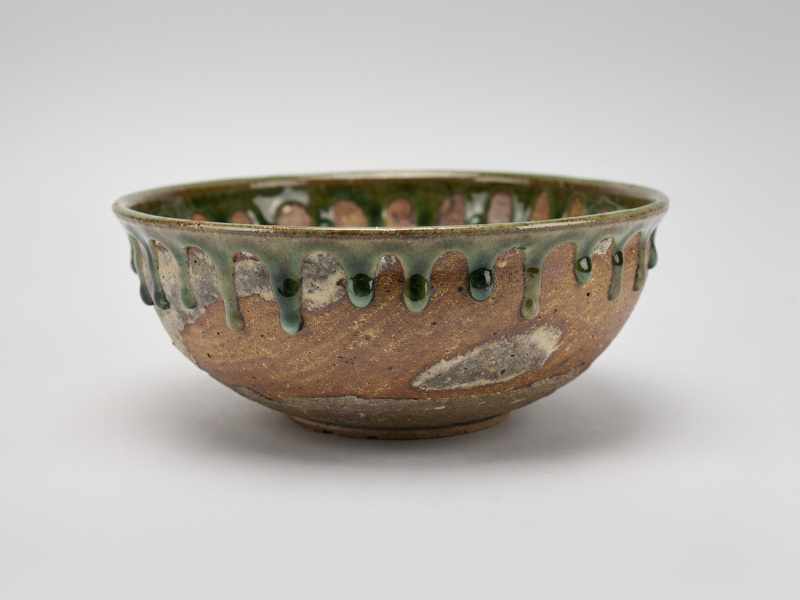 A wide stoneware bowl with a natural ash glaze, green glassy drips running down from the rim over warm brown clay.