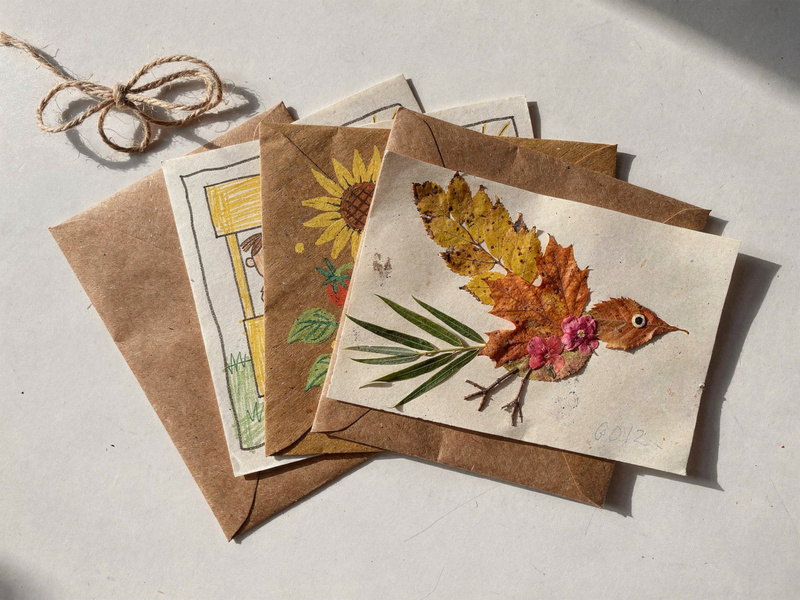 Folded note cards fanned out on brown kraft envelopes with a loop of twine. The front card shows the Leaf Bird collage, with the garden and lemonade cards behind it.