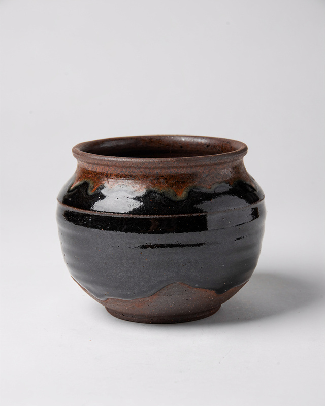 A black stoneware vessel with a glossy tenmoku glaze that breaks to rust brown on the edges and the rim.