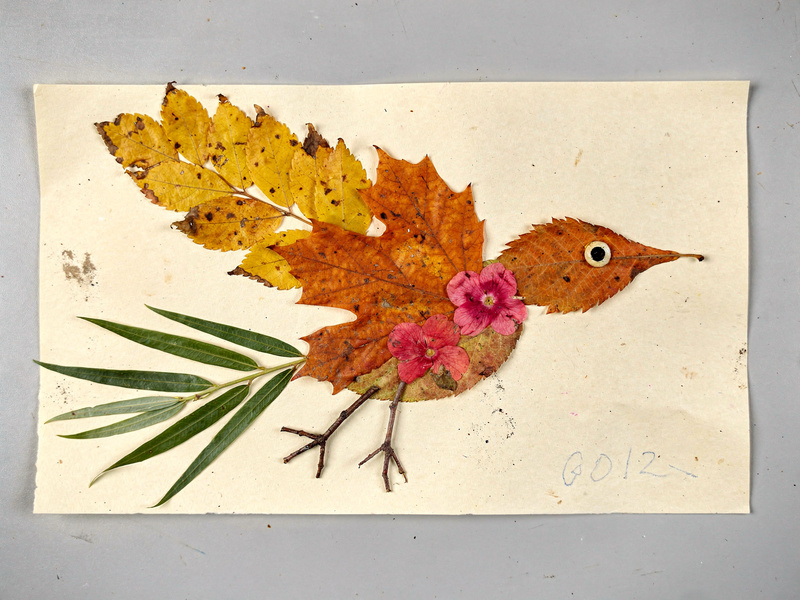 Collage of a bird in flight made of pressed leaves: a wing of yellow aspen leaves, an orange maple-leaf body, a willow-leaf tail, petal chest, and a sunflower-seed eye.