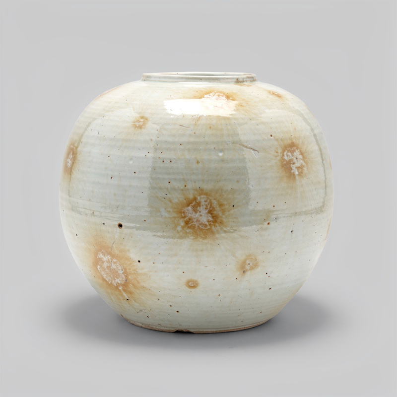 A large round white porcelain moon jar, slightly irregular in shape, creamy glaze with warm pooled spots.