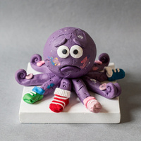 Purple clay octopus with worried eyebrows; six arms wear painted clay socks, one wears a real striped baby sock, and one arm is bare.