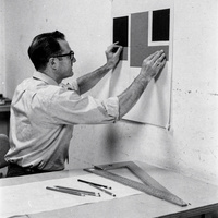 Tomas Ekwall at his drafting table, 1966. A black and white photograph from the 1960s of a man in his thirties with glasses and rolled shirt sleeves, seated at a drafting table in a sparse studio, pinning a study of black, red and grey rectangles to the wall, a T-square and pencils on the table.